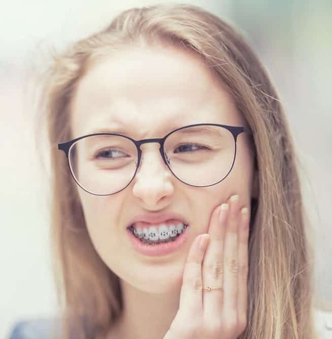 Young woman wearing glasses smiling with hand to cheek, indoor portrait setting.