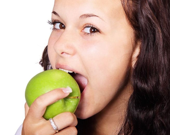 Woman biting green apple against white background, healthy eating concept