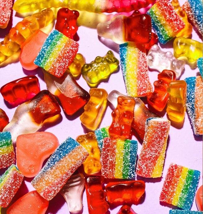 Colorful gummy bears and rainbow sour candy strips on pink background illustrating foods to avoid.