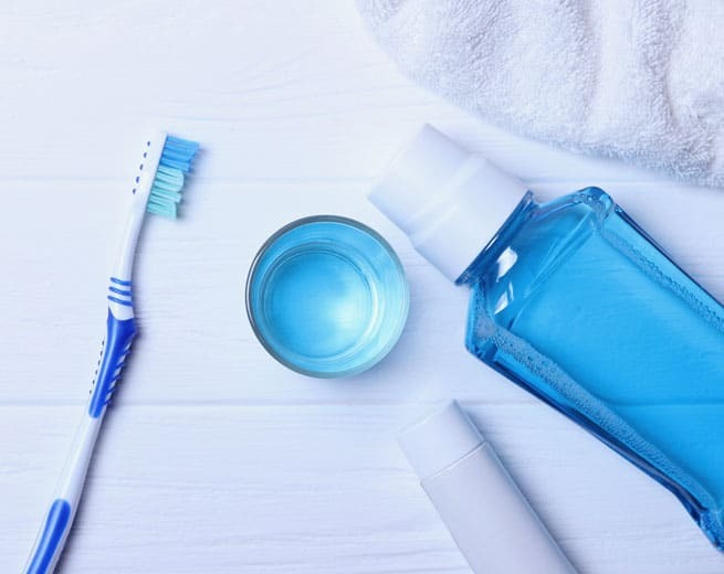 Blue toothbrush, mouthwash cup, and rinse bottle arranged on white towel for oral hygiene routine.