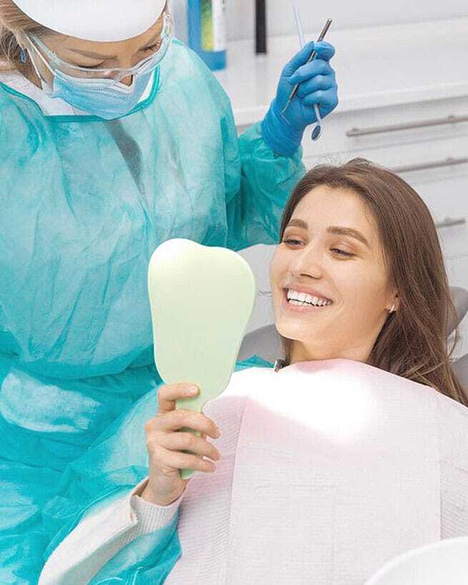 Smiling patient holding mirror while dentist prepares for scaling and root planing treatment.