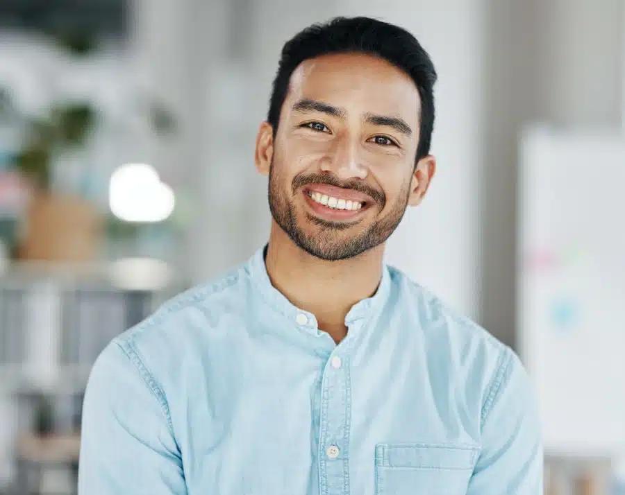 Professional man in light blue shirt smiling at camera in modern office environment
