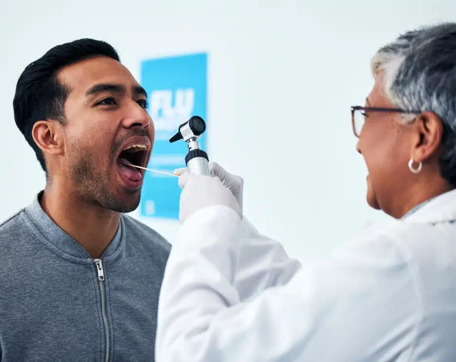 Medical professional examining patient's throat with otoscope in clinical setting.